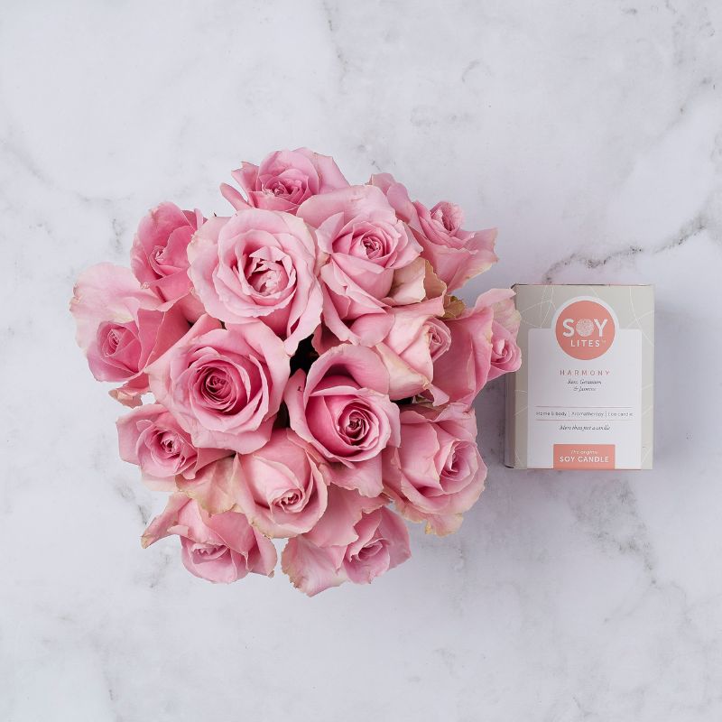 Top-down view of an elegant arrangement of pink roses with a SOY Lites Harmony candle on a marble background