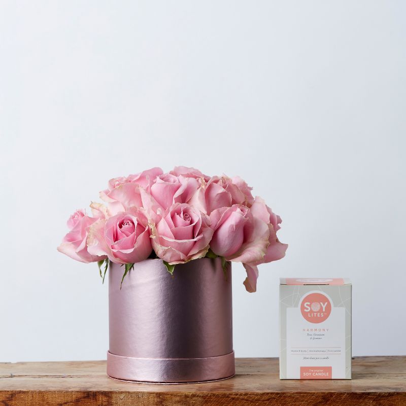 Pink rose arrangement in a blush-coloured cylinder vase beside a SOY Lites Harmony candle, displayed on a wooden surface