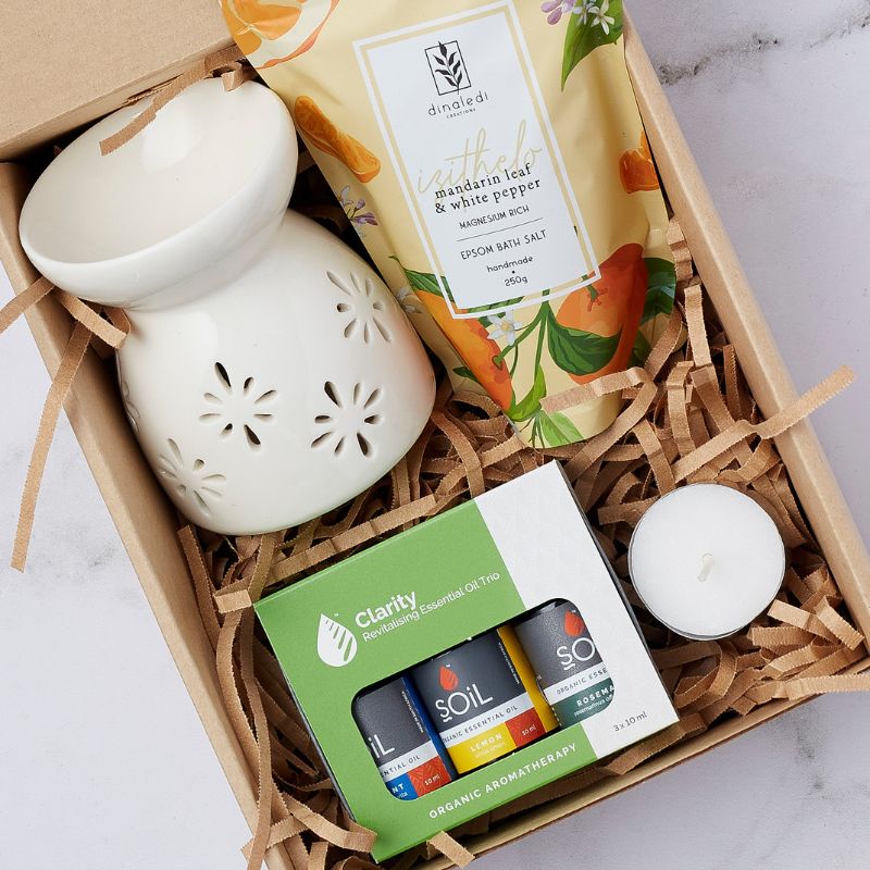 Close-up of ceramic oil burner, mandarin leaf & white pepper Epsom bath salt, Clarity essential oil trio, and tealight candle arranged in a gift box.