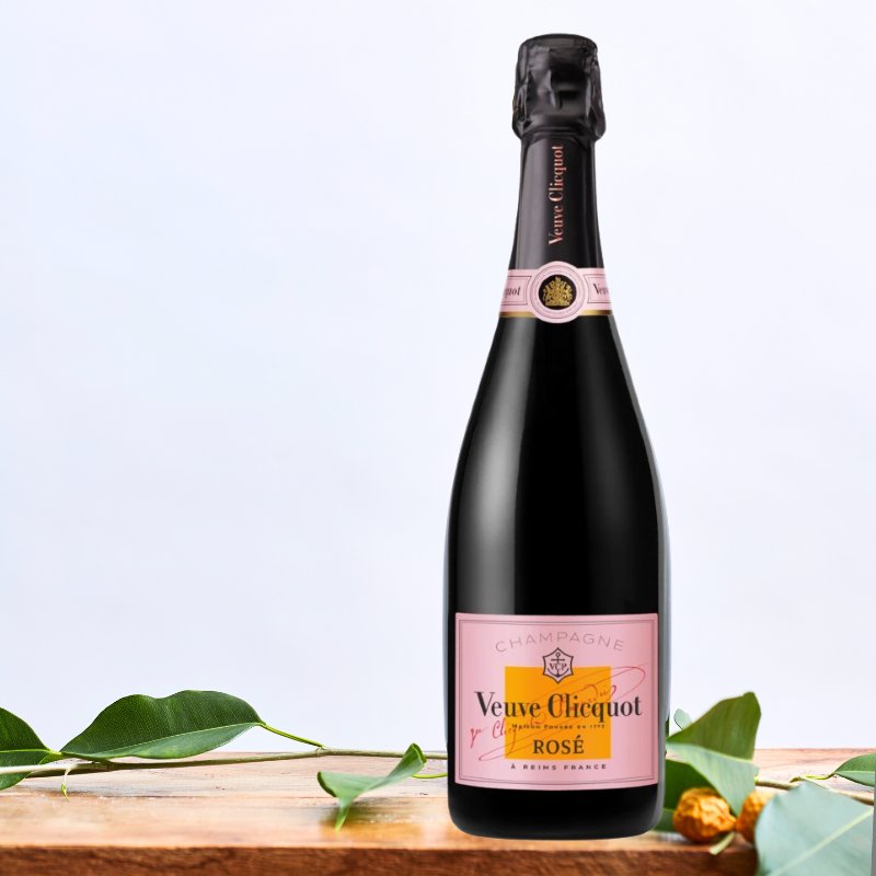 Veuve Clicquot Rosé champagne bottle with a signature pink label, elegantly displayed on a wooden table with green foliage.