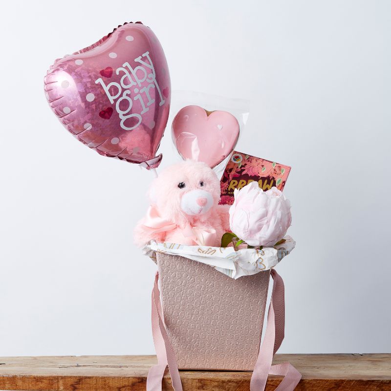 Pink baby girl gift hamper with plush teddy, pink heart balloon, flower, chocolate, and pink heart-shaped cookie