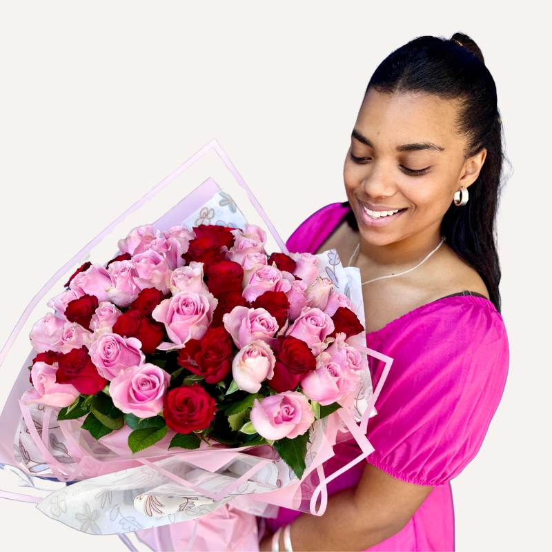 Smiling woman holding a bouquet of pink and red roses wrapped in delicate floral paper and pink ribbon by Fabulous Flowers & Gifts.