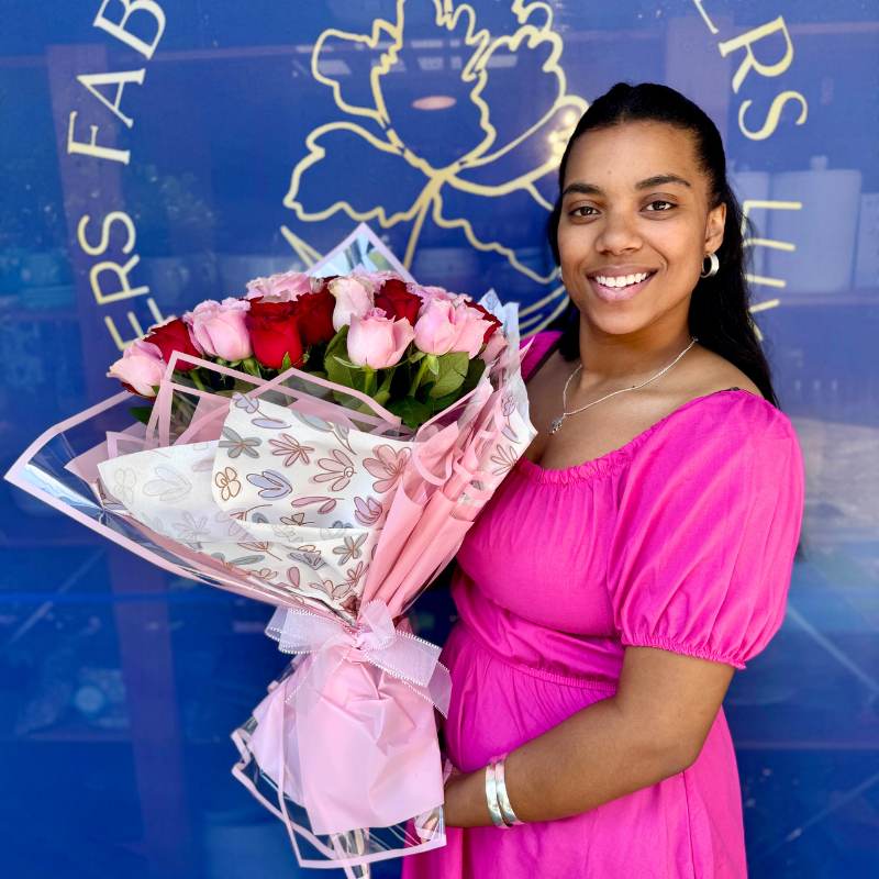 Woman in a pink dress holding a vibrant bouquet of pink and red roses, posed in front of the Fabulous Flowers & Gifts logo.