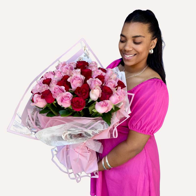 Elegant bouquet of pink and red roses in a smiling woman’s hands, wrapped with floral detailing and pink accents.