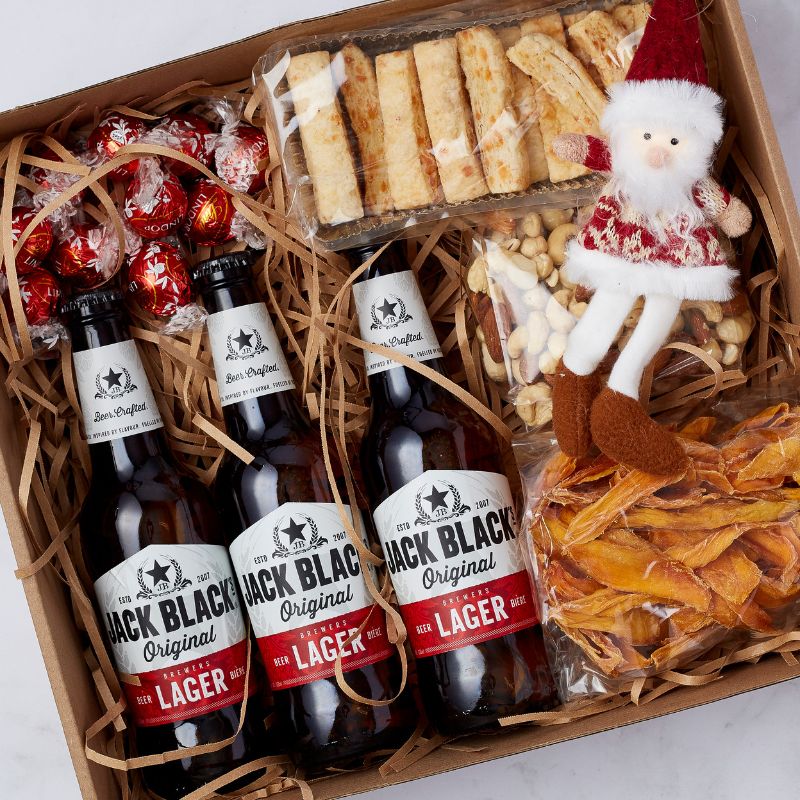 Festive gift box with Jack Black Lager, assorted snacks, Lindt chocolates, dried mango, mixed nuts, breadsticks, and Santa figurine