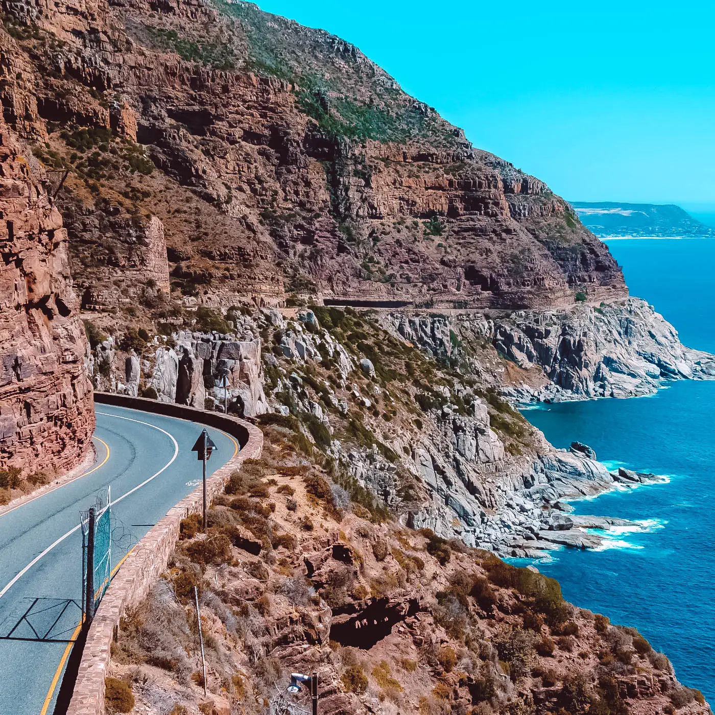 Scenic coastal road winding along rugged cliffs with ocean views under a clear blue sky. Fabulous Flowers and Gifts. Cape Town.