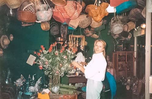 Josie van Aswegen, founder of Fabulous Flowers and Gifts, arranging a bouquet of roses in her quaint shop filled with hanging baskets.