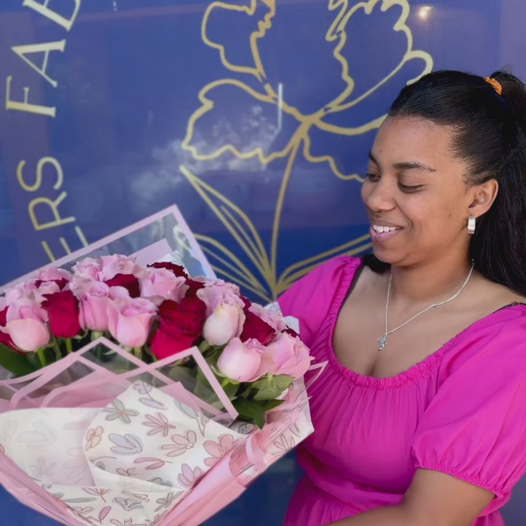 A showcase of the Whispers of the Heart bouquet featuring pink and red roses in a feminine wrap, held by a smiling woman.