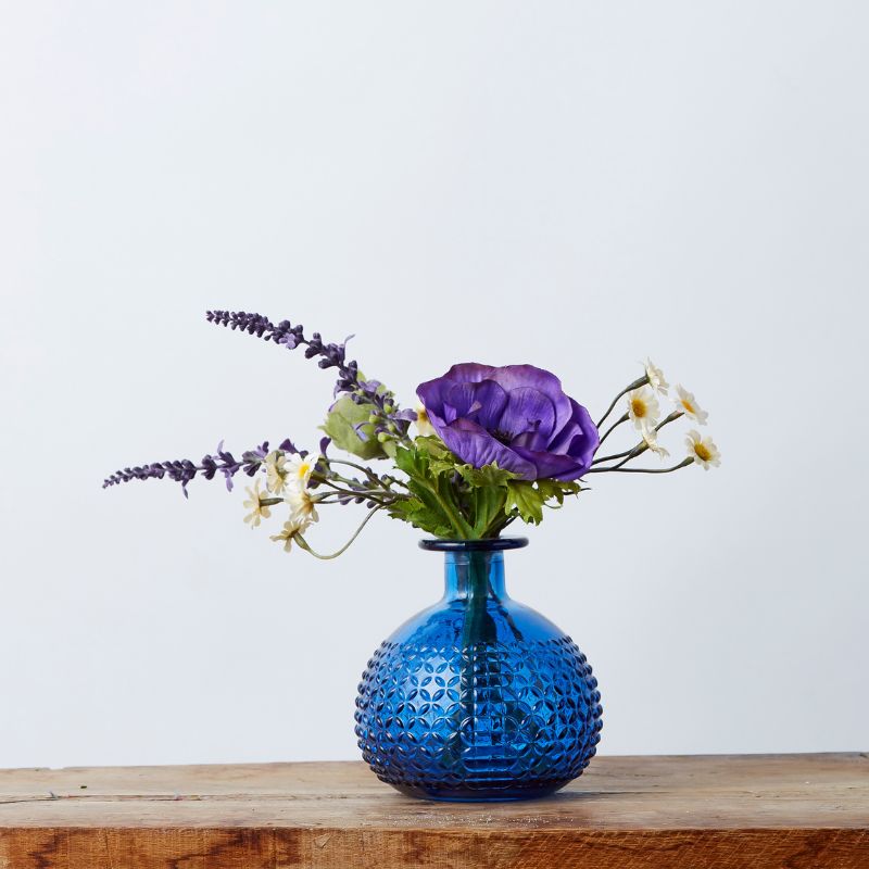 Infinite Blue Silk Arrangement featuring vibrant silk hydrangeas, delphiniums, bougainvillaea, and more in a decorative blue vase, displayed on a wooden surface.