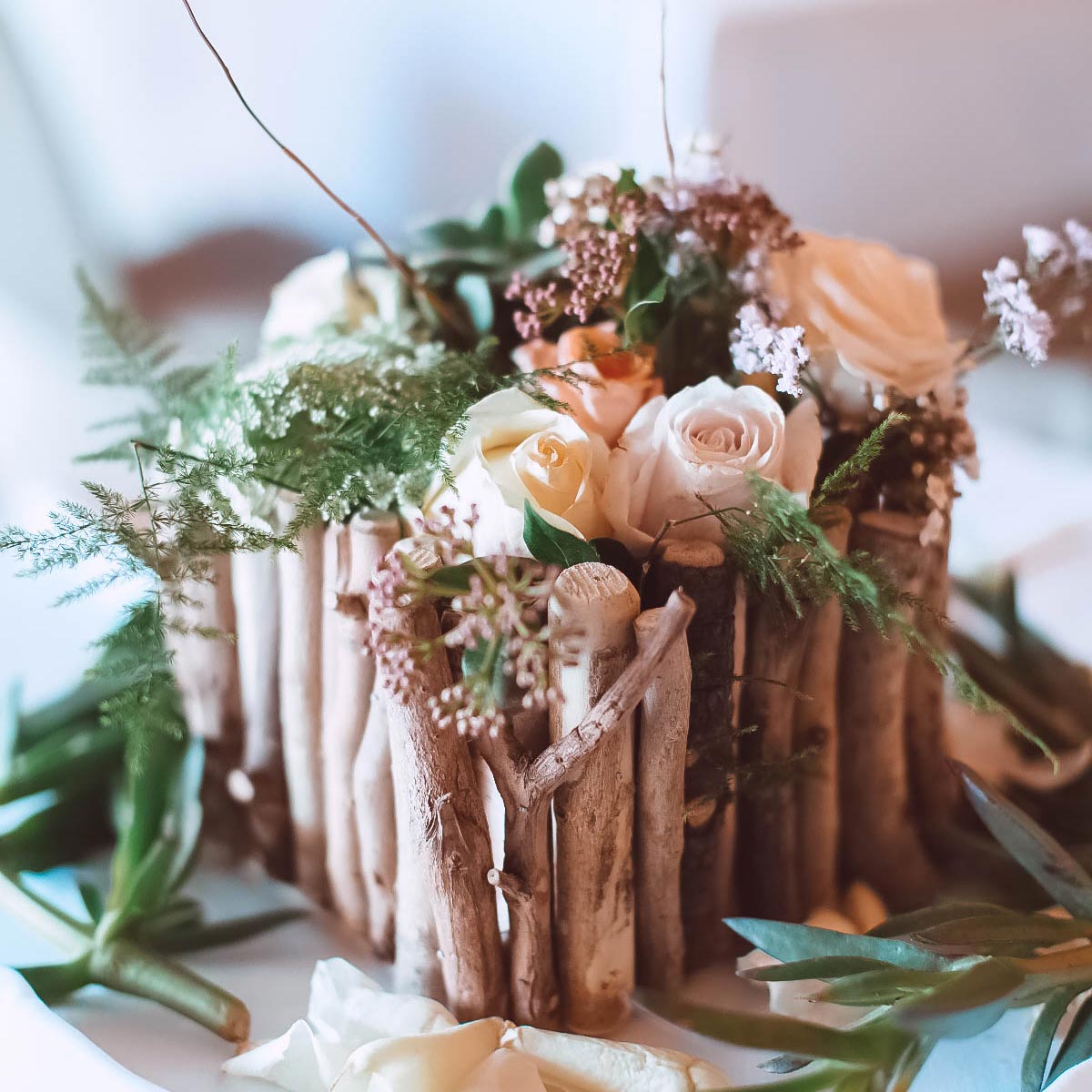 Rustic floral centrepiece with white roses and greenery arranged in a wooden twig holder, perfect for weddings. Fabulous Flowers and Gifts.