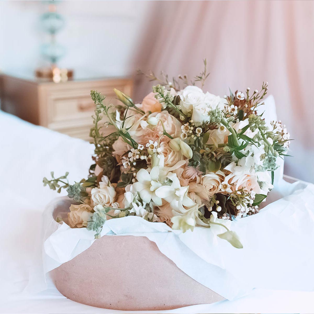 Romantic wedding bouquet with delicate white and blush flowers arranged in a soft pink vase, placed on a white cloth. Fabulous Flowers and Gifts. Weddings.