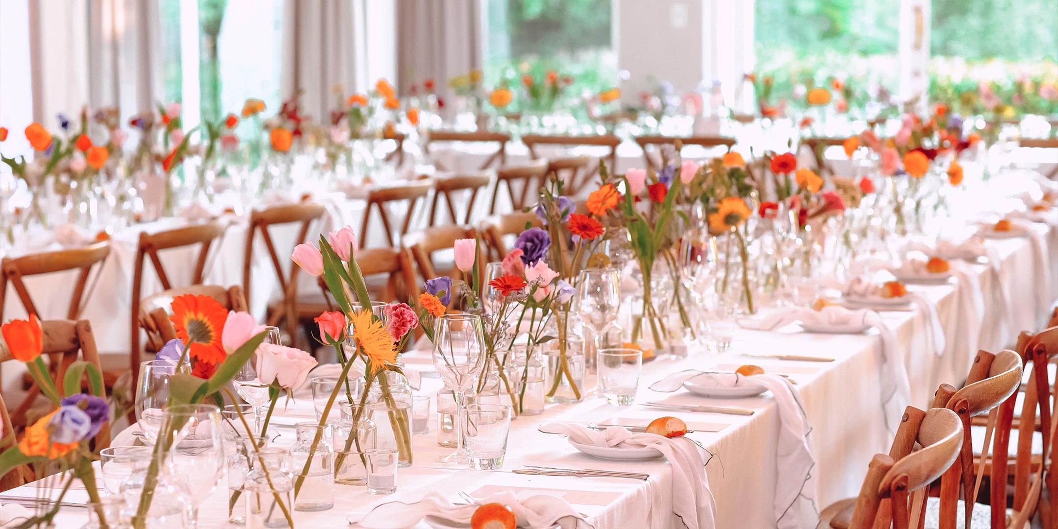 Elegant wedding reception setup with long tables adorned with colourful floral arrangements and wooden chairs. Let's chat about making your wedding day perfect. Weddings. Fabulous Flowers and Gifts.