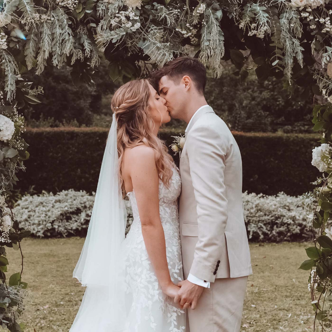 Bride and groom sharing a kiss under a floral arch in a garden setting. High-Quality Flower Arrangements. Fabulous Flowers and Gifts. Weddings.